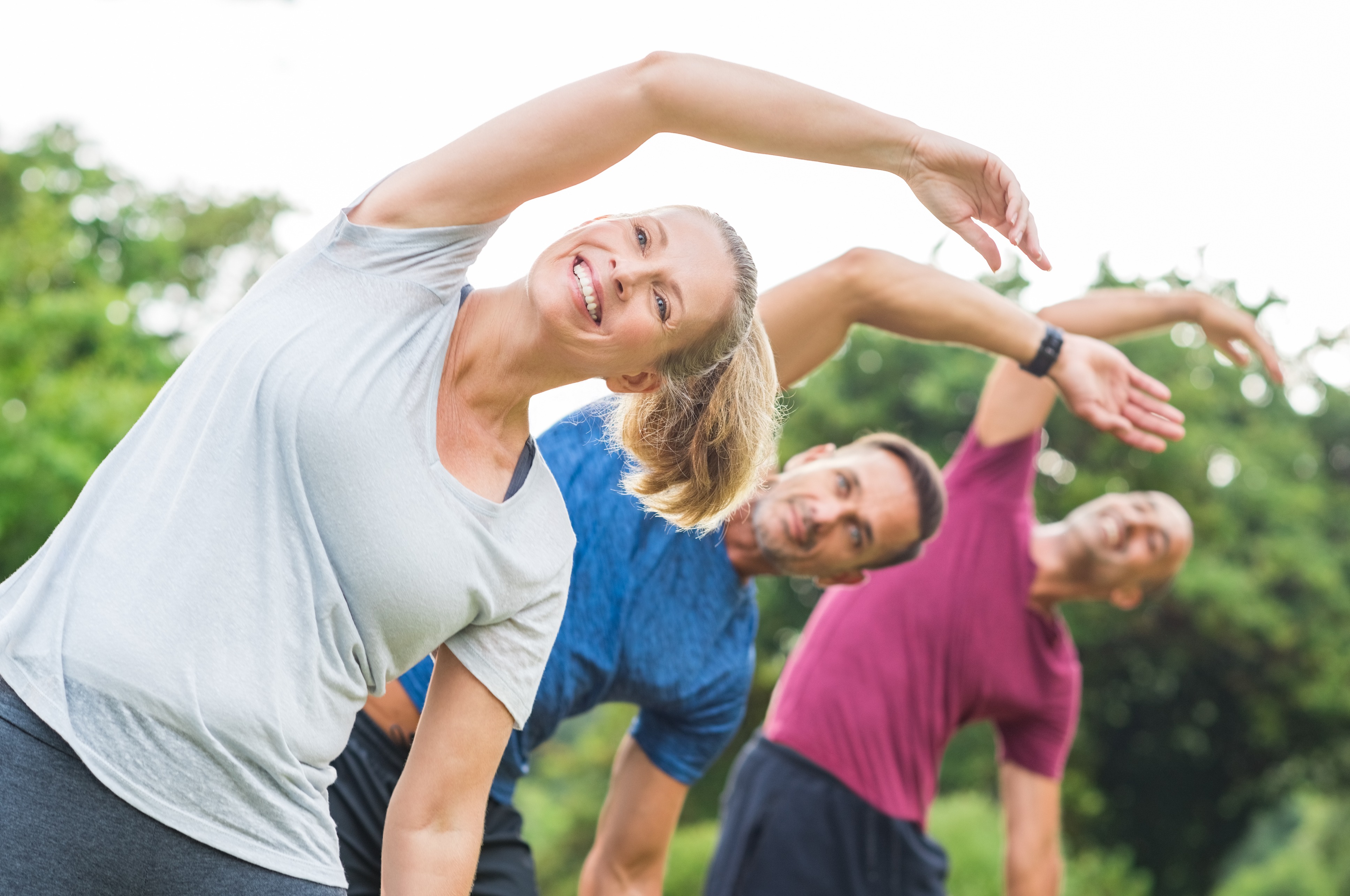 Smiling men and women stretching together outdoors on a bright summer day