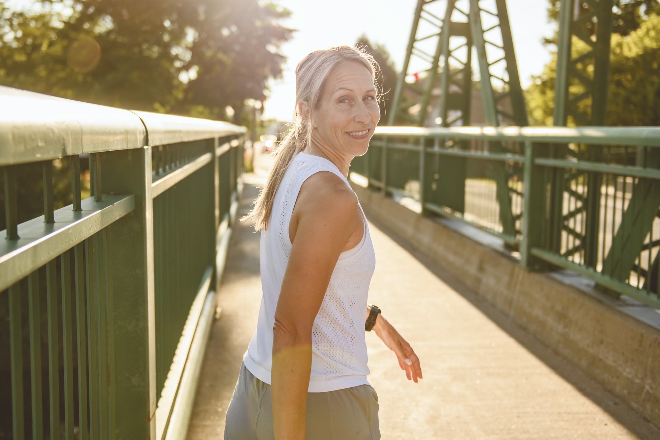 A relaxed, smiling woman pausing during an evening walk on a bridge